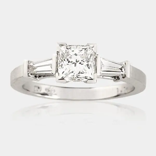 Handmade, three stone engagement ring in 18ct white gold with princess cut diamond in picture frame setting and two tapered baguette diamonds.