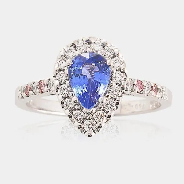Handmade, 18ct white gold halo-style engagement ring featuring pear shape sapphire surrounded by round brilliant cut diamonds. Pink diamonds and white diamonds are set into the band.