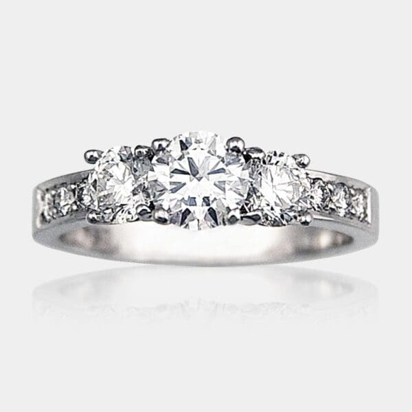 Round brilliant cut three stone diamond engagement ring with diamond shoulders set in white gold.