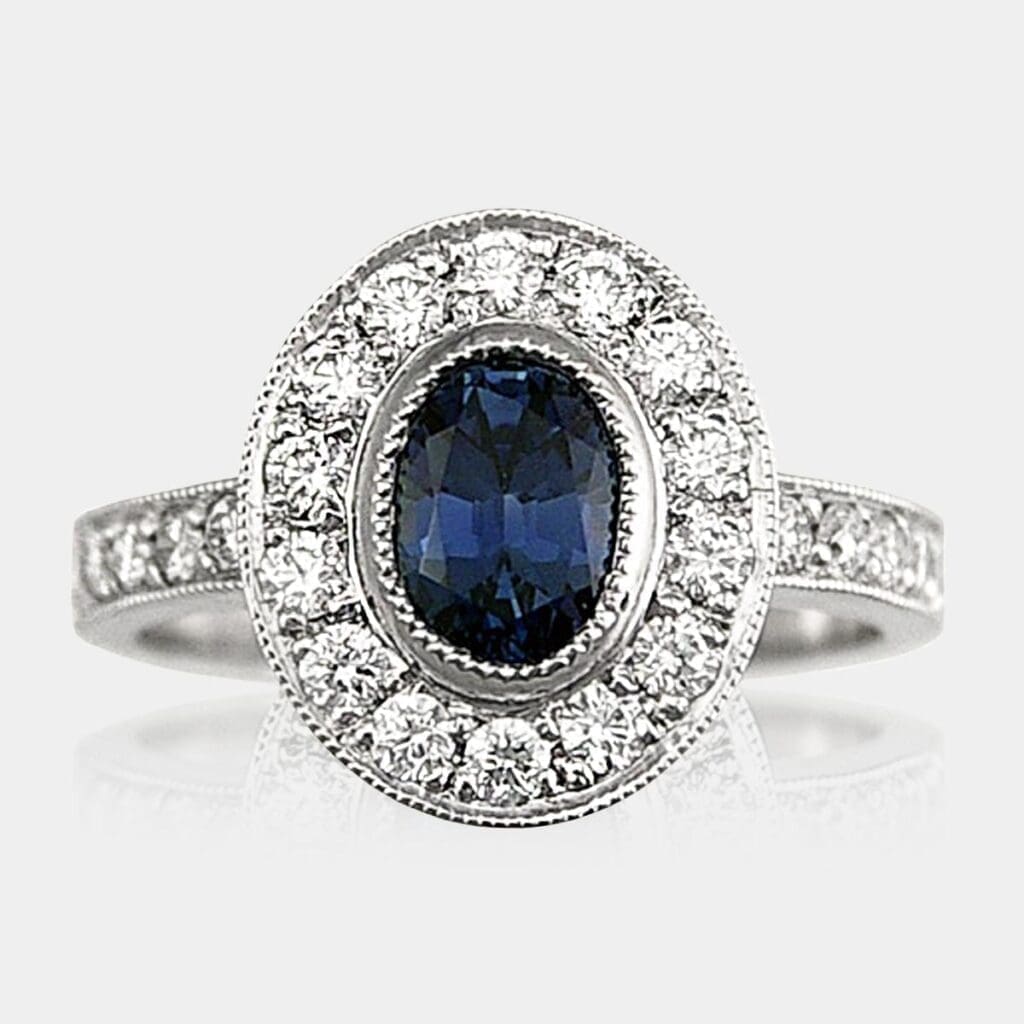 Oval cut Australian blue sapphire ring with round brilliant cut diamond halo and diamonds in the band, with milgrain detail.
