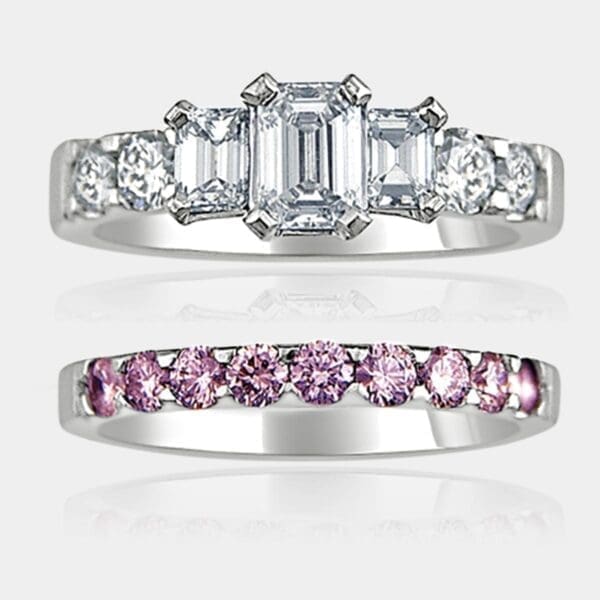 3 stone emerald cut diamond ring with round brilliant cut shoulder diamonds and matching pink diamond wedding ring.