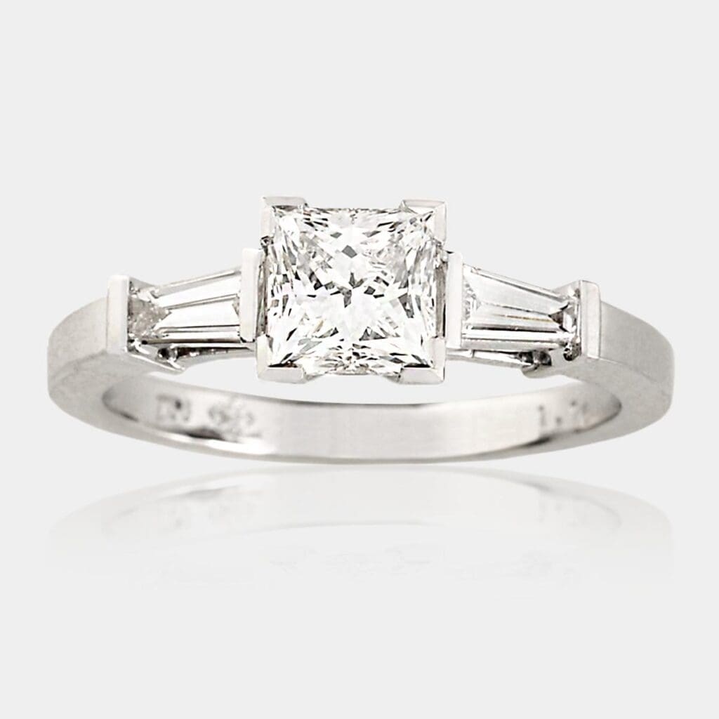 Handmade, three stone engagement ring in 18ct white gold with princess cut diamond in picture frame setting and two tapered baguette diamonds.