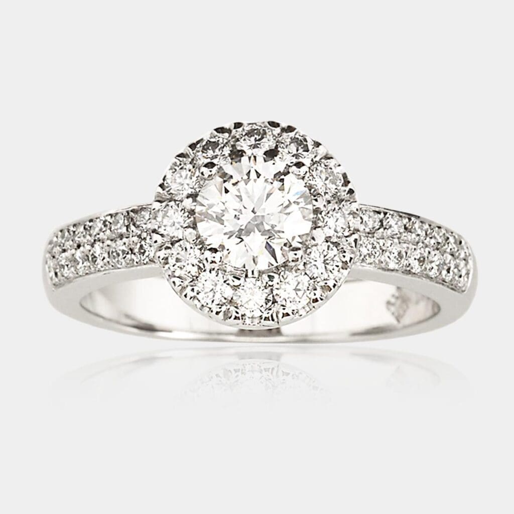 Halo style engagement ring with round brilliant cut diamond in the centre, surrounded by round diamonds with two rows of diamonds in the shoulders.