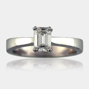 Emerald cut solitaire diamond engagement ring with tapered white gold band.
