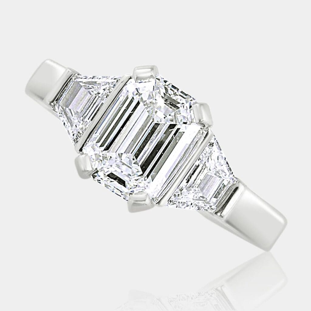 Three-stone engagement ring featuring emerald cut diamond with tapered baguette diamonds on either side, set in 18ct white gold.