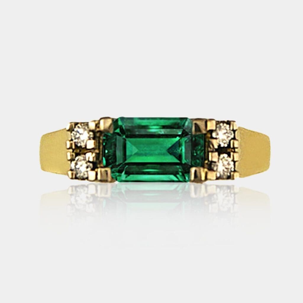 Handmade dress ring featuring emerald cut green emerald and round brilliant cut diamonds in 18ct yellow gold.