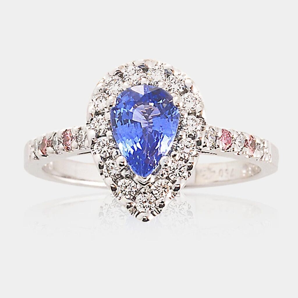 Handmade, 18ct white gold halo-style engagement ring featuring pear shape sapphire surrounded by round brilliant cut diamonds. Pink diamonds and white diamonds are set into the band.