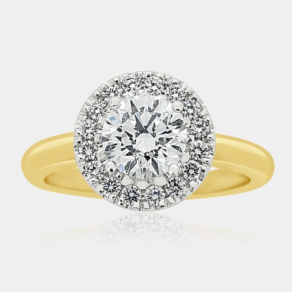 Two-tone, yellow gold ring featuring round brilliant cut centre diamond and halo of round diamonds in a white gold setting.