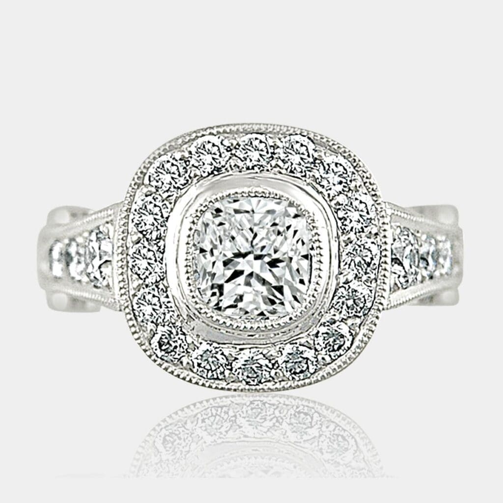 Cushion cut diamond ring with surround and shoulder diamonds.