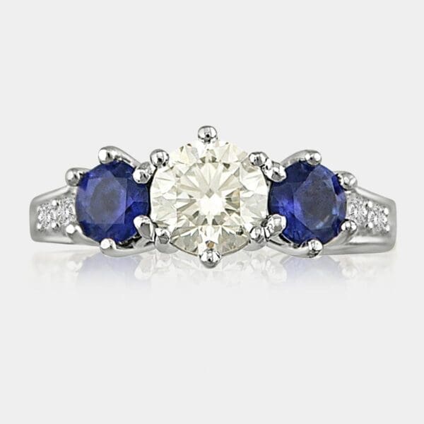 Three stone ring with one round brilliant cut diamond in the centre and two round cut blue sapphires on the side.