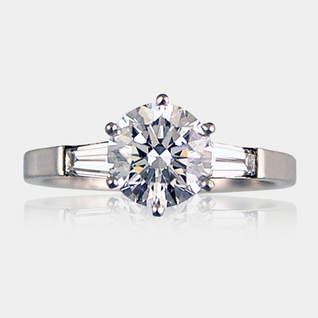 Round brilliant cut diamond engagement ring with tapered baguette diamonds on each side, set in 18ct white gold.