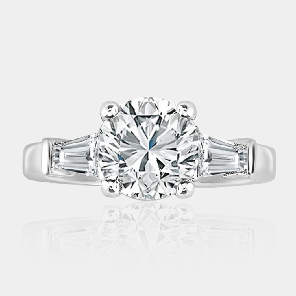 Three-stone round brilliant cut diamond engagement ring with four-claw setting and tapered baguette cut diamonds on the side.