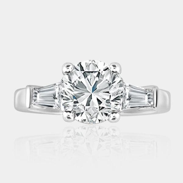 Three-stone round brilliant cut diamond engagement ring with four-claw setting and tapered baguette cut diamonds on the side.